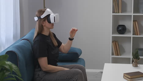 female-gamer-is-using-HMD-display-sitting-on-couch-in-living-room-modern-technology-of-virtual-reality-woman-is-gesticulating-by-hands-device-of-future